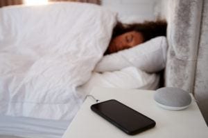 Woman Asleep on a smart mattress with Virtual Assistant and Smartphone on Bedside Table - in What are Smart Mattresses & Smart Beds? - by Simply Good Sleep