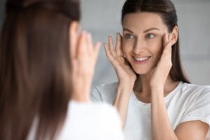 Well-Slept Woman Looking in the Mirror at her Beautiful Glowing Skin - Simply Good Sleep