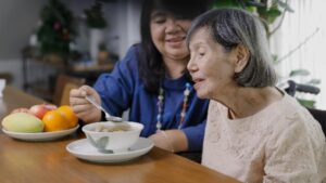 Female Caregiver Feeding Elderly Woman - Caregiver can benefit from Sleep Tips for Caregivers outlined in blog for amazing sleep - Simply Good Sleep