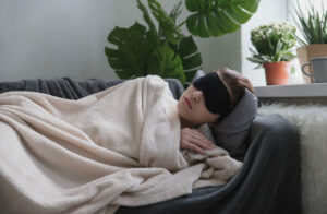 Woman wearing a sleep mask naps on the couch during the day - in the post Why Napping is Good for You - by Simply Good Sleep